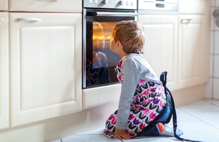 young boy kneeling in front of oven looking at what is baking inside.