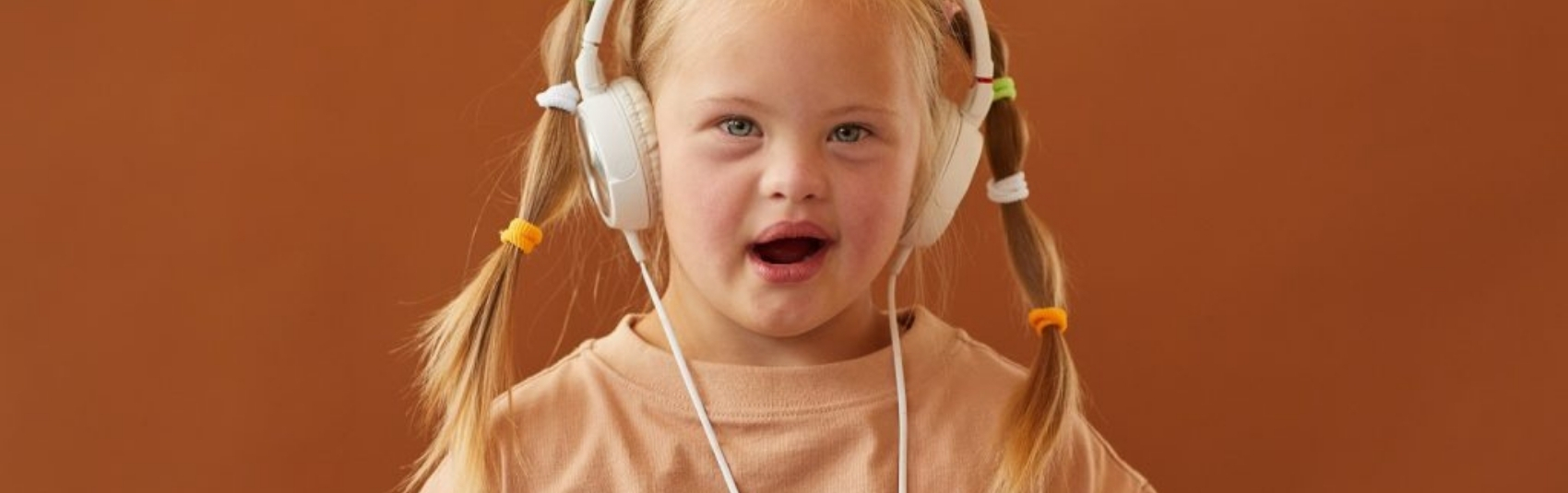 young girl with blonde hair holding iPad and listening to music using over the ear headphones