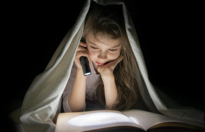 Child reading a book by torchlight under the covers