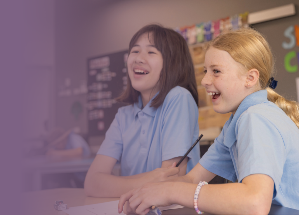 Two students laughing together in a classroom.