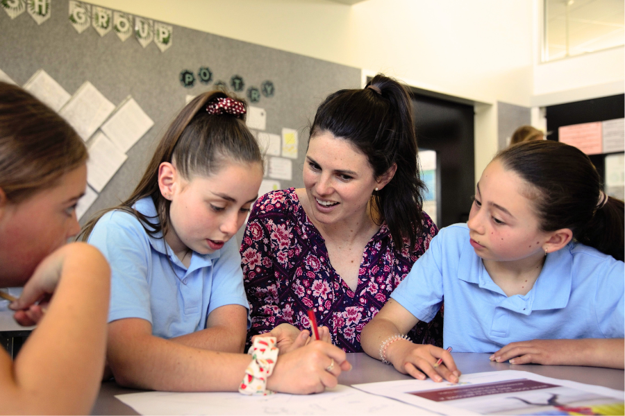 Teacher helping two students with their writing lesson